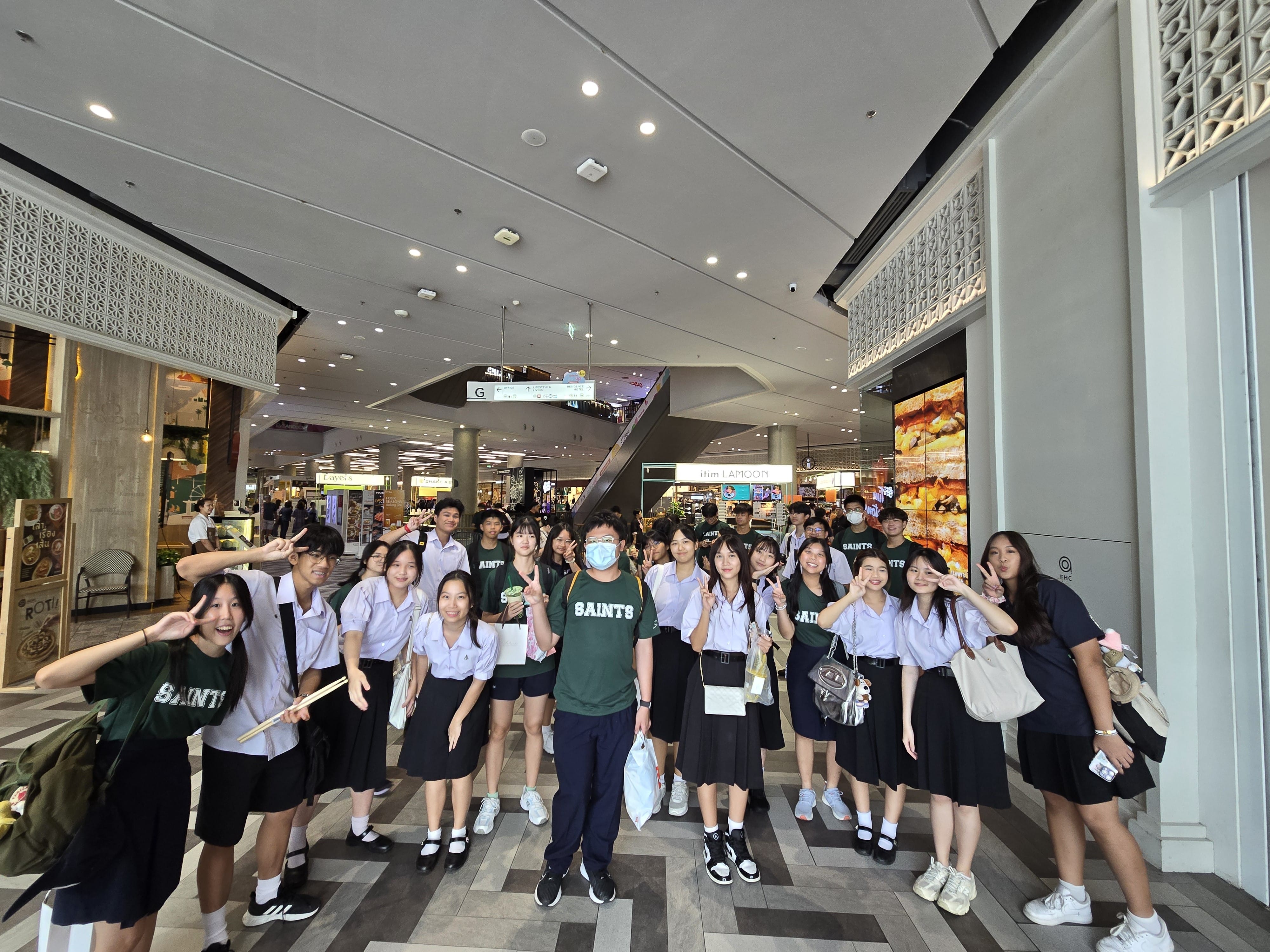 Students in St Andrew's Junior College 'Saints' jerseys and Thai school uniforms pose for a fun group photo at what appears to be a shopping mall in Bangkok.